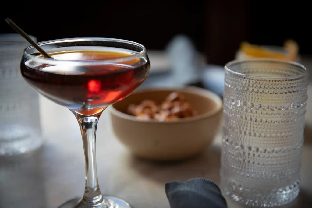 A dark red cocktail in a coupe glass with a stir stick.