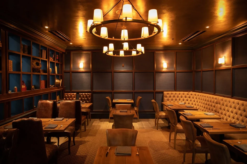 Luxurious restaurant with dark wood paneling, bookshelves, and two tiered chandeliers.