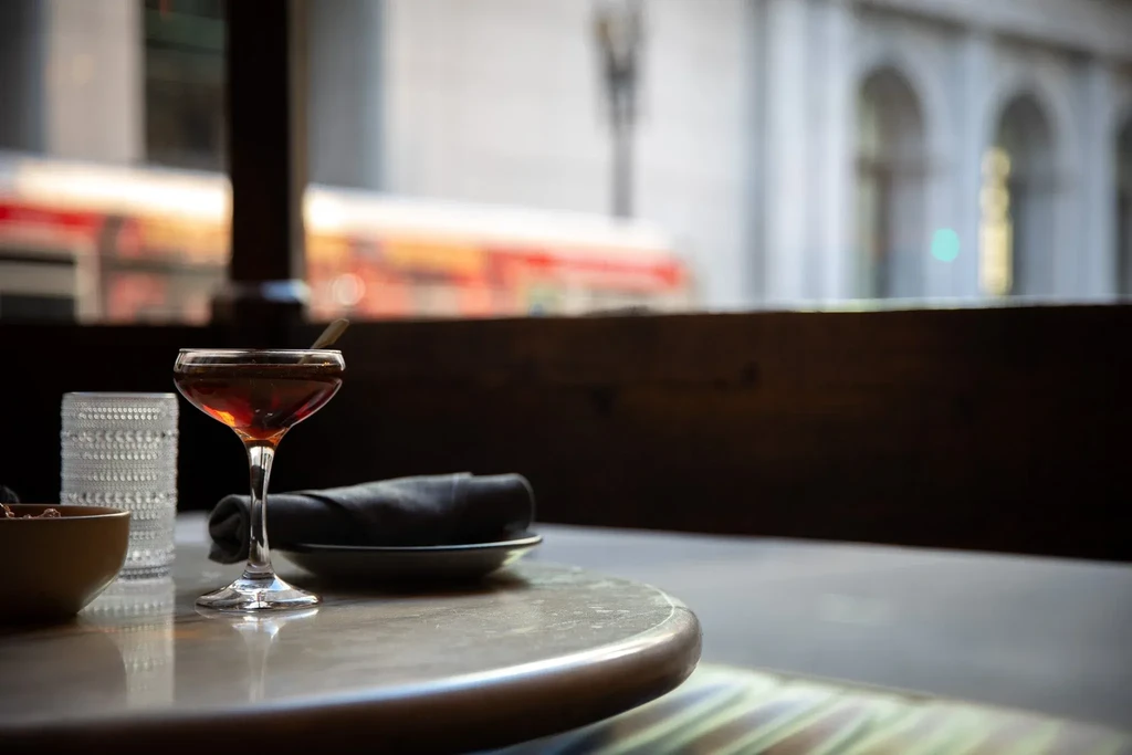 A cocktail on a marble table by a window with a city view.