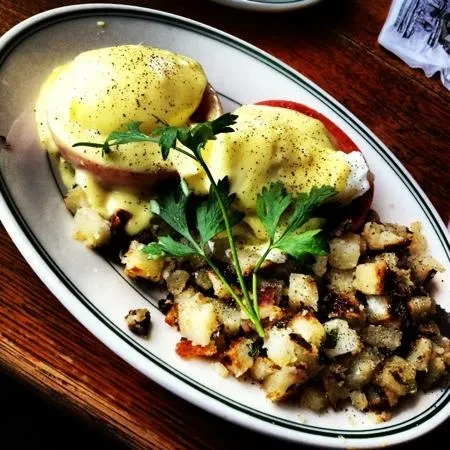 Two eggs Benedict and a side of home fries on a white plate.