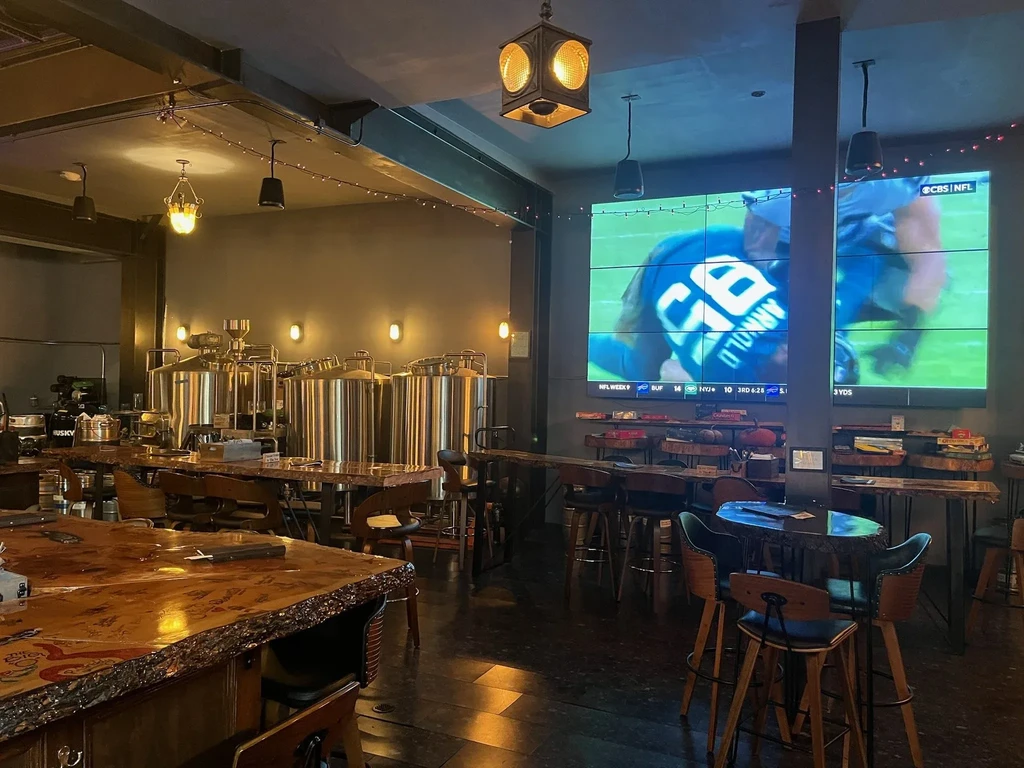 A bar with brewing tanks, wooden tables, and a large screen showing football.