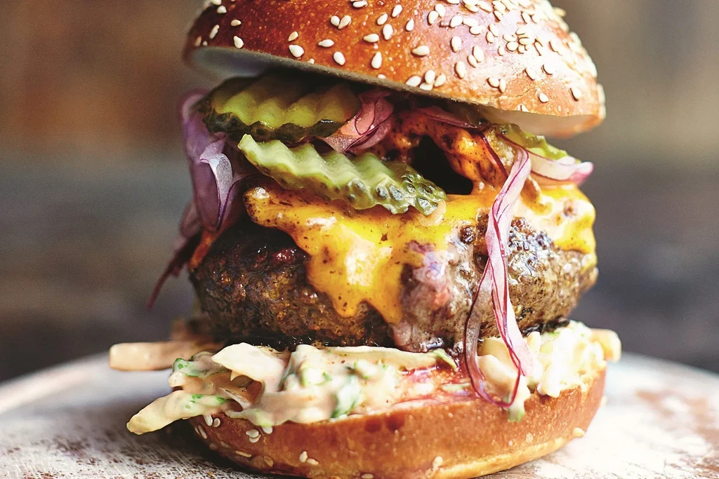 A close-up of a cheeseburger with pickles, red onions, and sauce.