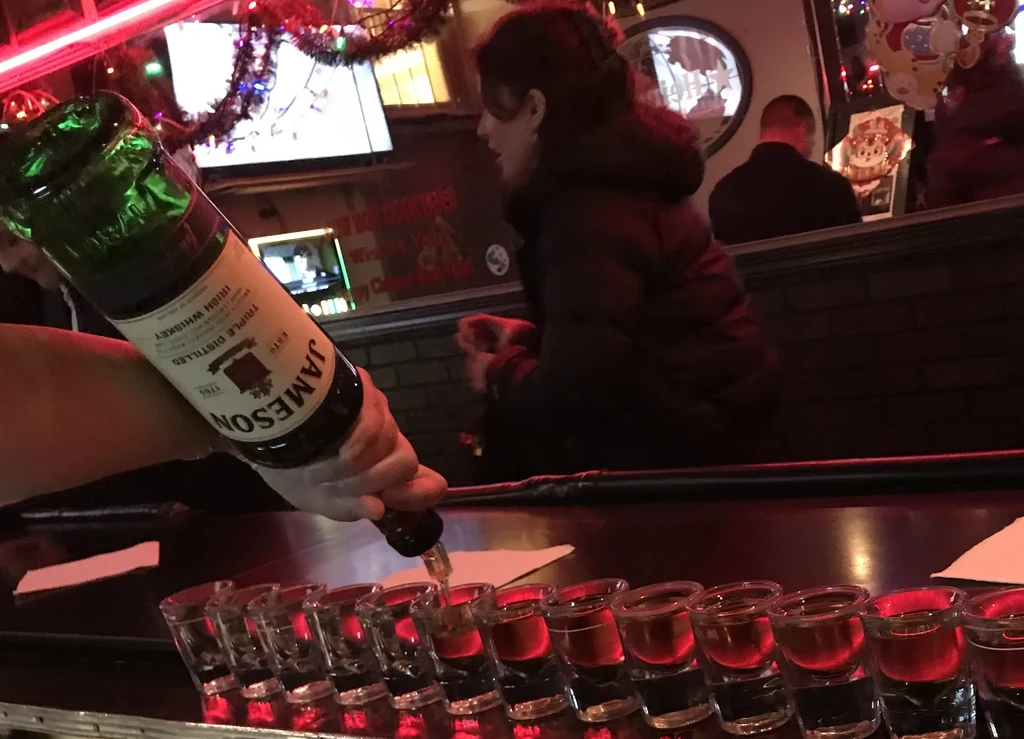 A person pours Jameson Irish Whiskey into a line of shot glasses at a bar.