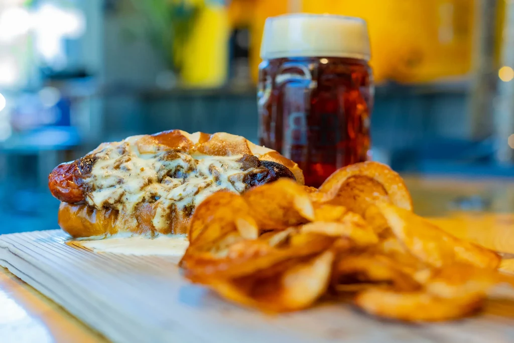 Grilled sausage with melted cheese and chips on a wooden board.
