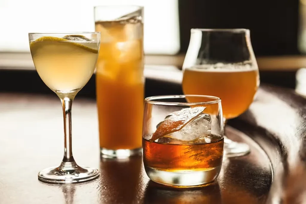 Four alcoholic beverages on a bar: cocktails, an old-fashioned, and beer.