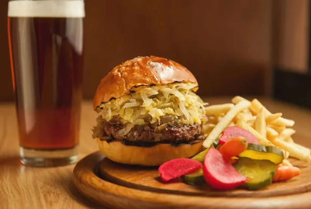 A burger with sauerkraut, fries, pickled vegetables, and a glass of beer.