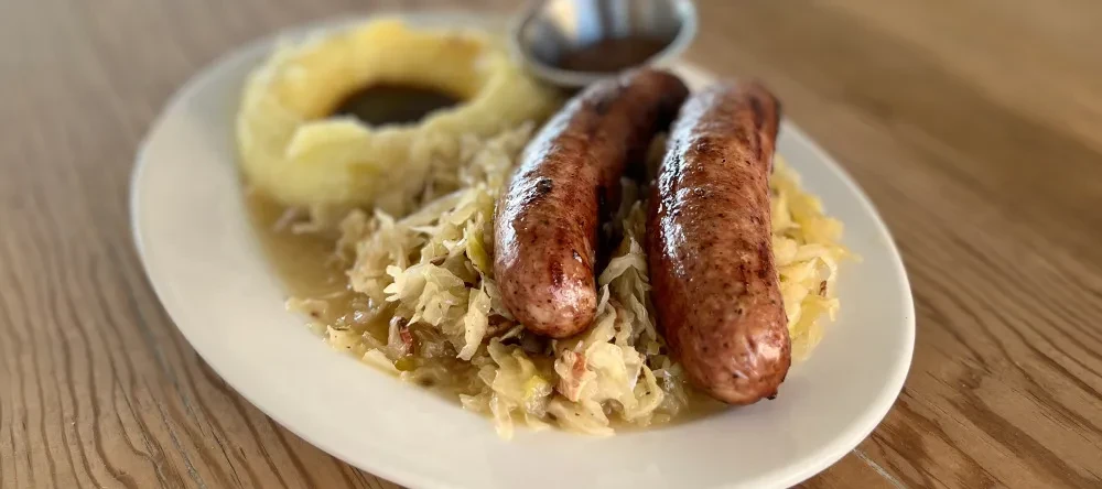 Two grilled sausages, sauerkraut, mashed potatoes, and gravy on a white plate.
