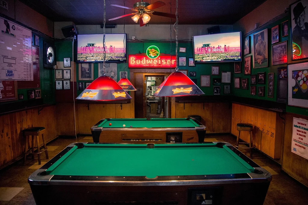 Pool hall with green walls, two pool tables, and Budweiser signs.