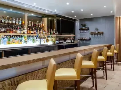 A long bar with stools and shelves of alcohol bottles.