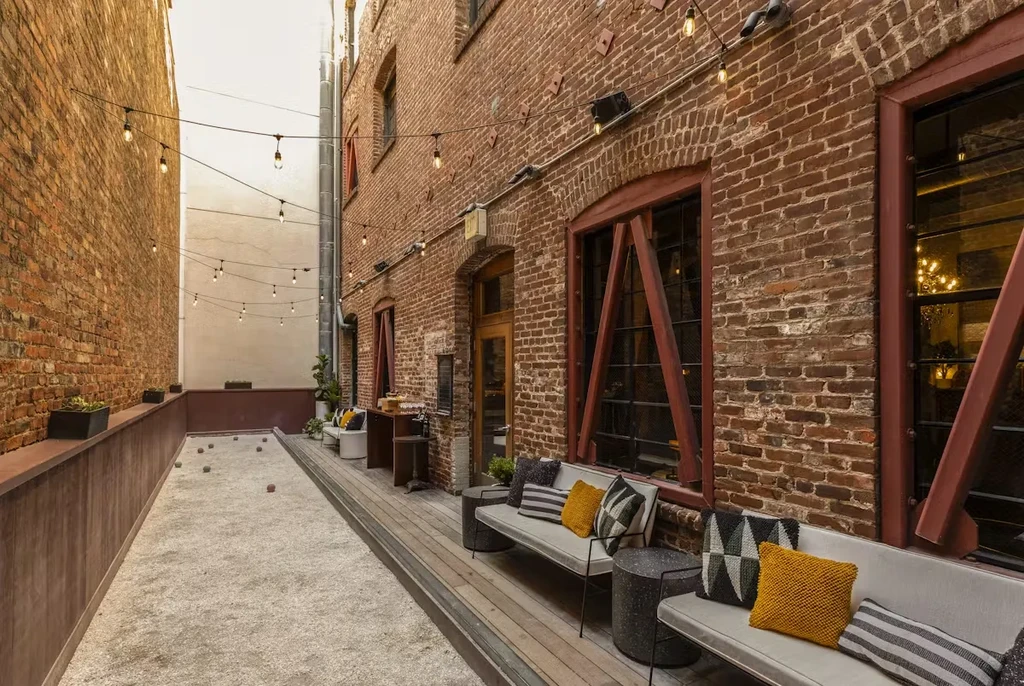 Outdoor alley bocce court with string lights and brick walls.