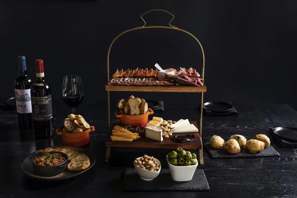 A two-tiered server displaying cheeses, cured meats, bread, olives, and nuts.