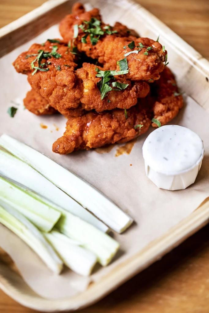 Fried chicken strips with sauce and celery sticks on a tray.