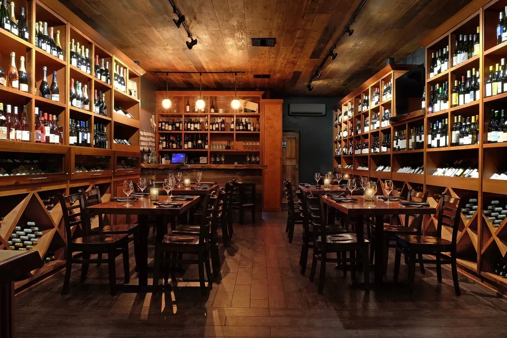 A restaurant with long wooden tables and high shelves of wine bottles.