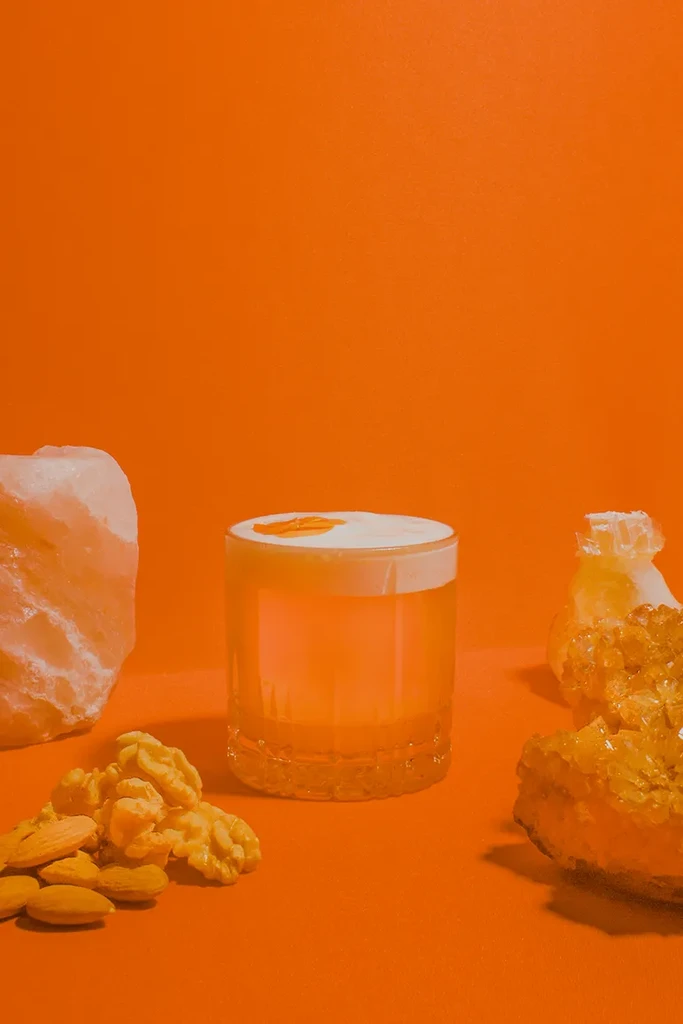 Orange cocktail with foam, walnuts, almonds, and crystals on orange background.