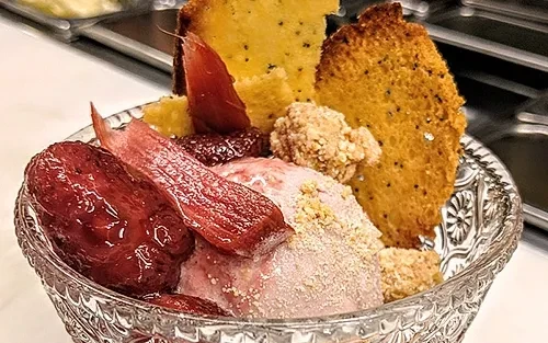 Dessert bowl with pink ice cream, roasted fruit, and poppy seed crisps.