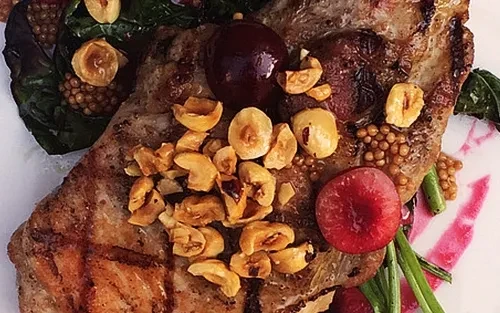 Grilled steak with hazelnuts, mustard seeds, and cranberries on a white plate.