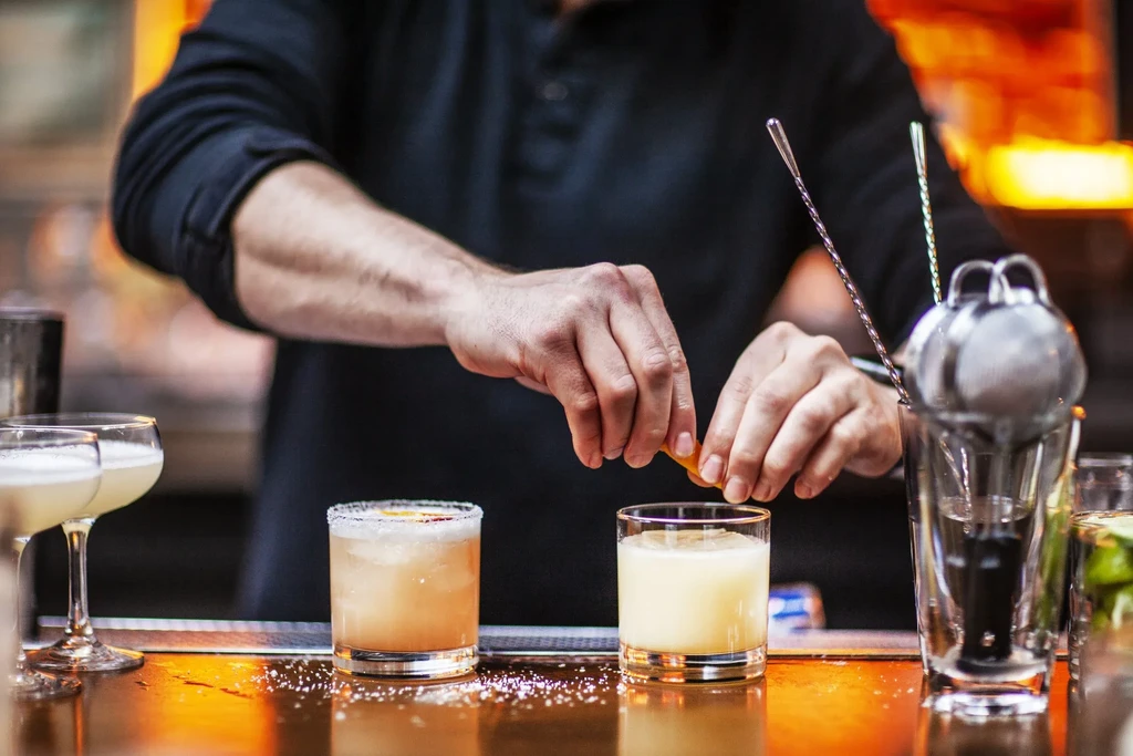Bartender garnishing a cocktail with an orange peel at a bar.