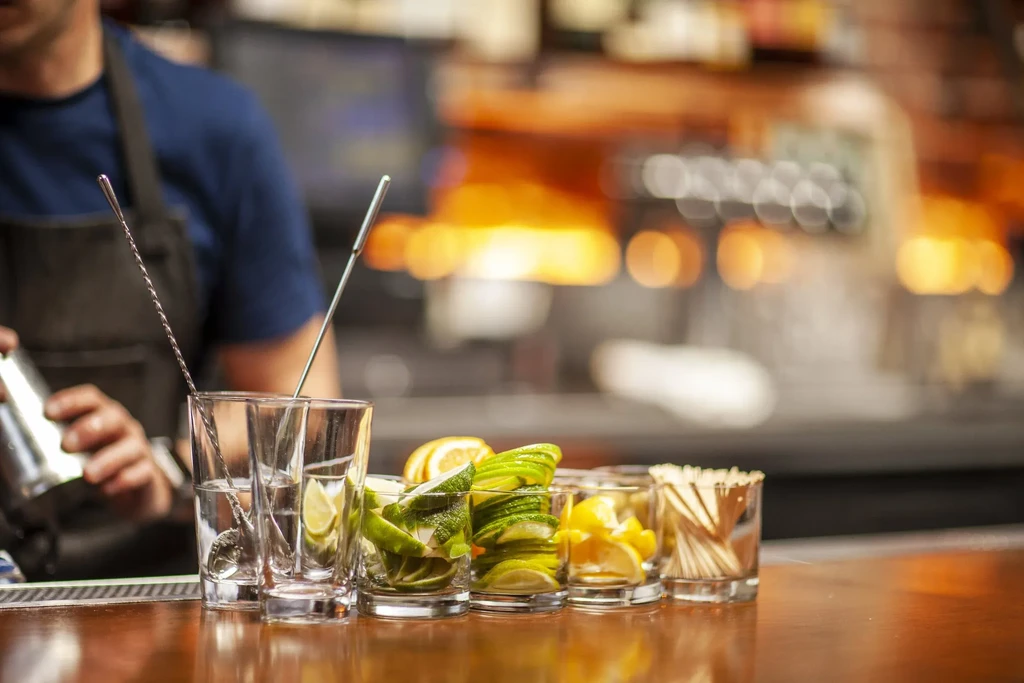Bartender shaking a drink with garnishes and tools on the bar.