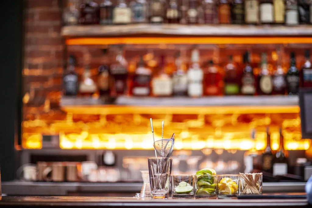 Bar counter with cocktail tools, sliced fruit, and liquor bottles.
