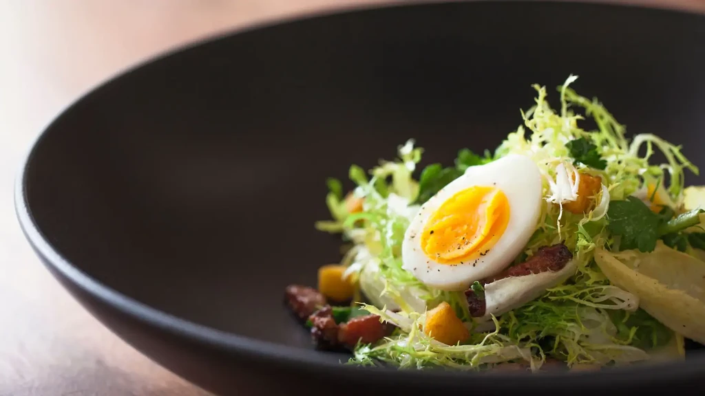 Salad with greens, bacon, egg, and croutons in a black bowl.