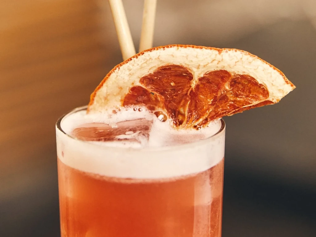 Close-up of a pink frothy cocktail garnished with a dried orange slice.