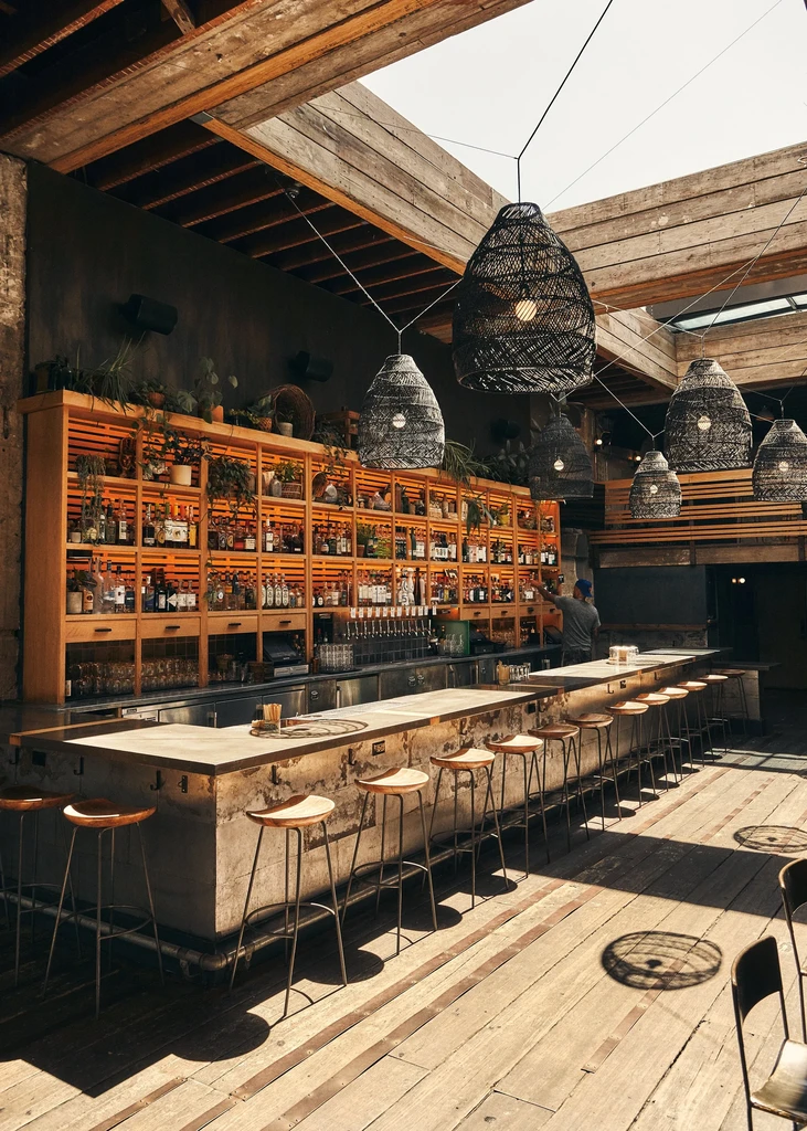 An industrial-style bar with a wooden floor, high stools, and a full liquor shelf.