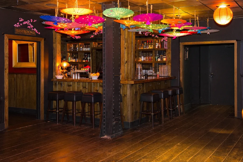 An empty bar with colorful hanging parasol lights and a black metal beam.
