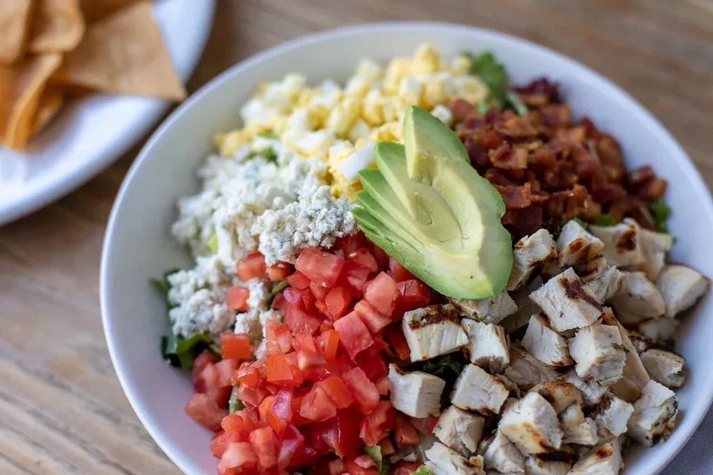 A close-up of a Cobb salad with chicken, avocado, bacon, and cheese.