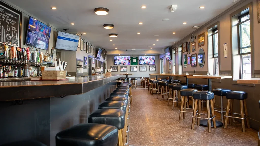 An empty bar with a long counter and rows of stools and tables.