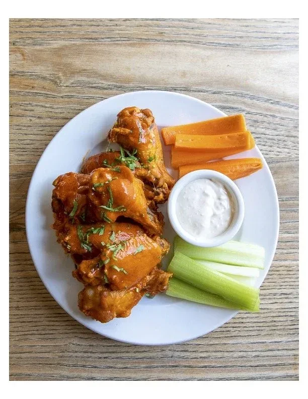 Chicken wings, carrots, celery, and dip on a white plate.