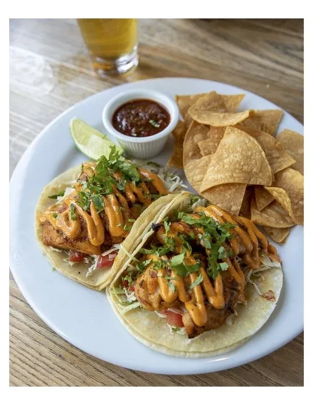 Two fish tacos with chips, salsa, and a lime on a plate.
