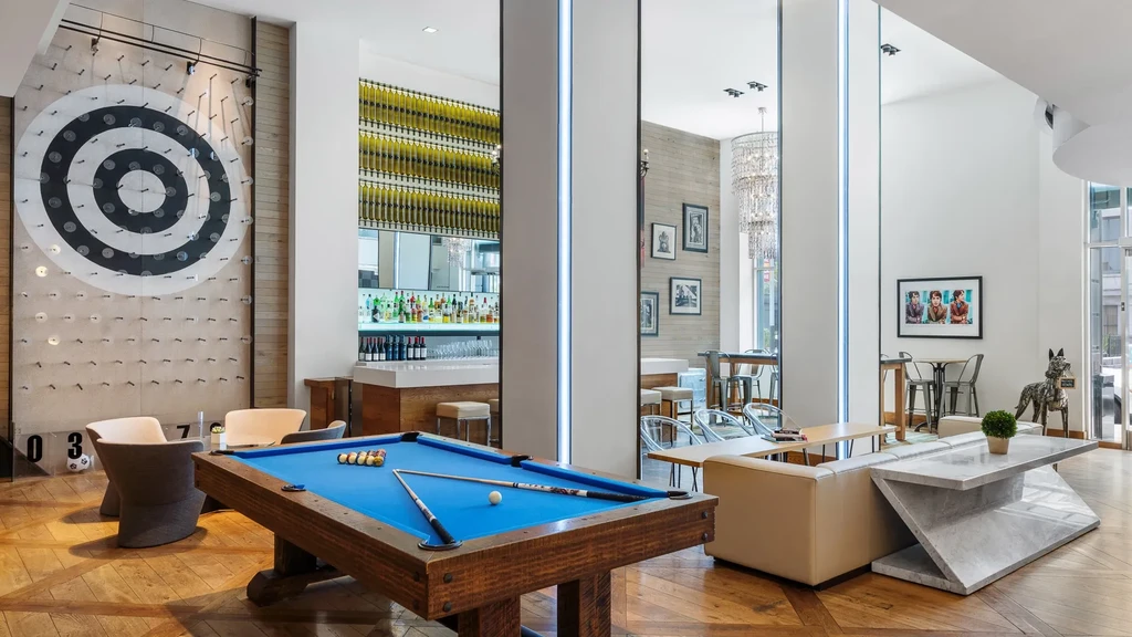A modern game room with a pool table, bar, and dartboard art.