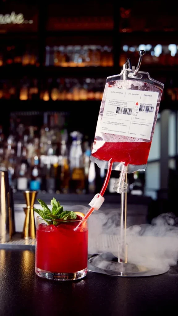 A cocktail served from a blood bag into a glass with mint.