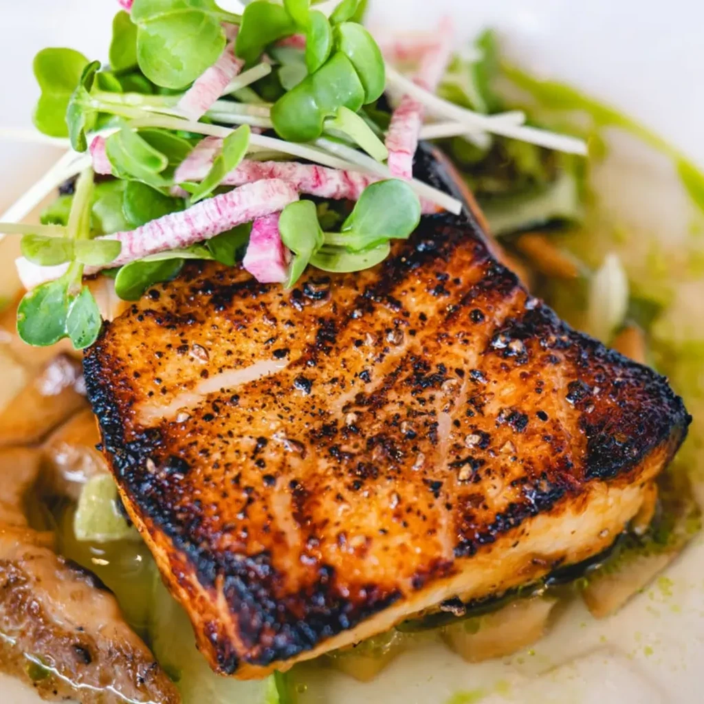 A seared piece of fish with microgreens and sliced radishes on top.
