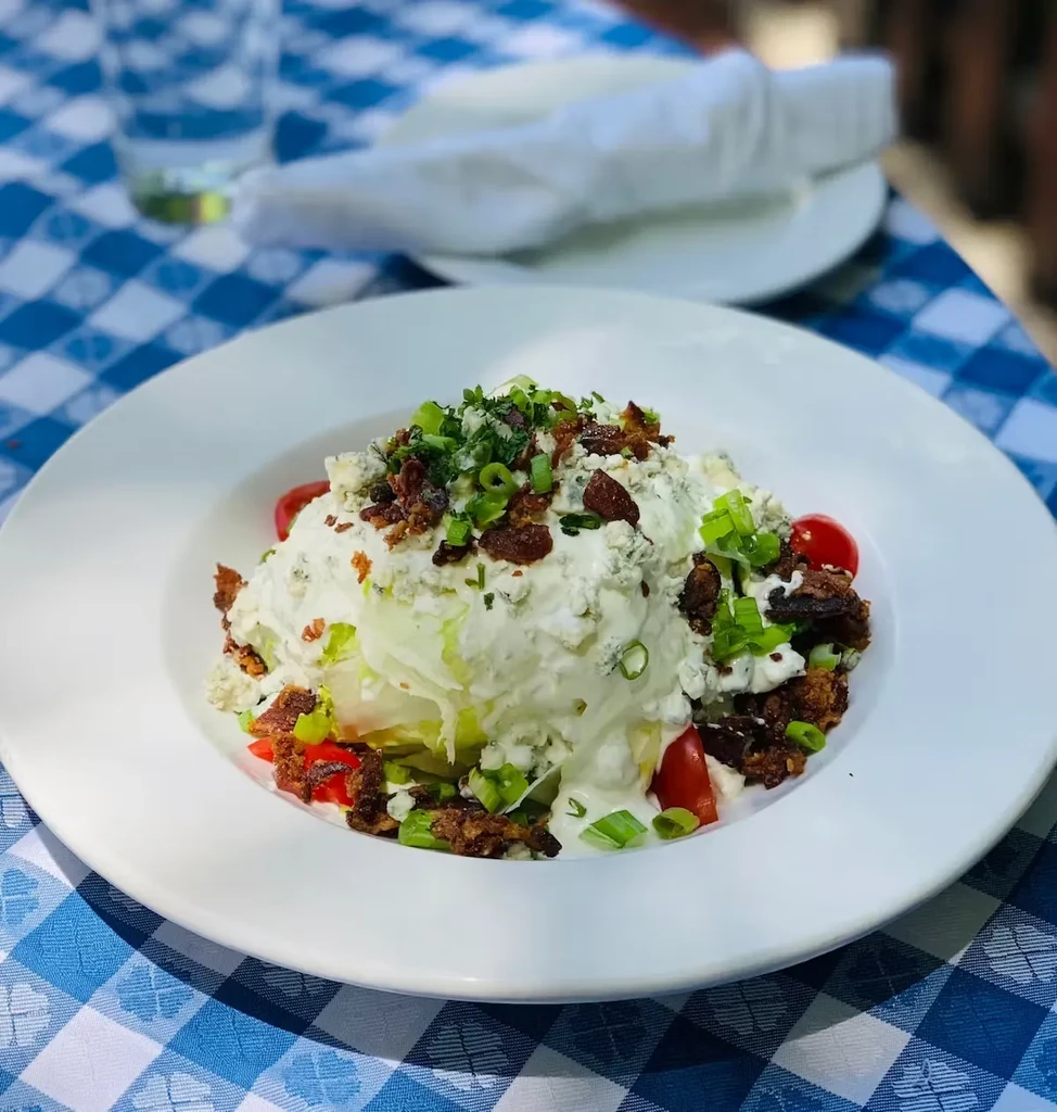 Wedge salad with blue cheese, bacon, and cherry tomatoes on a checked tablecloth.