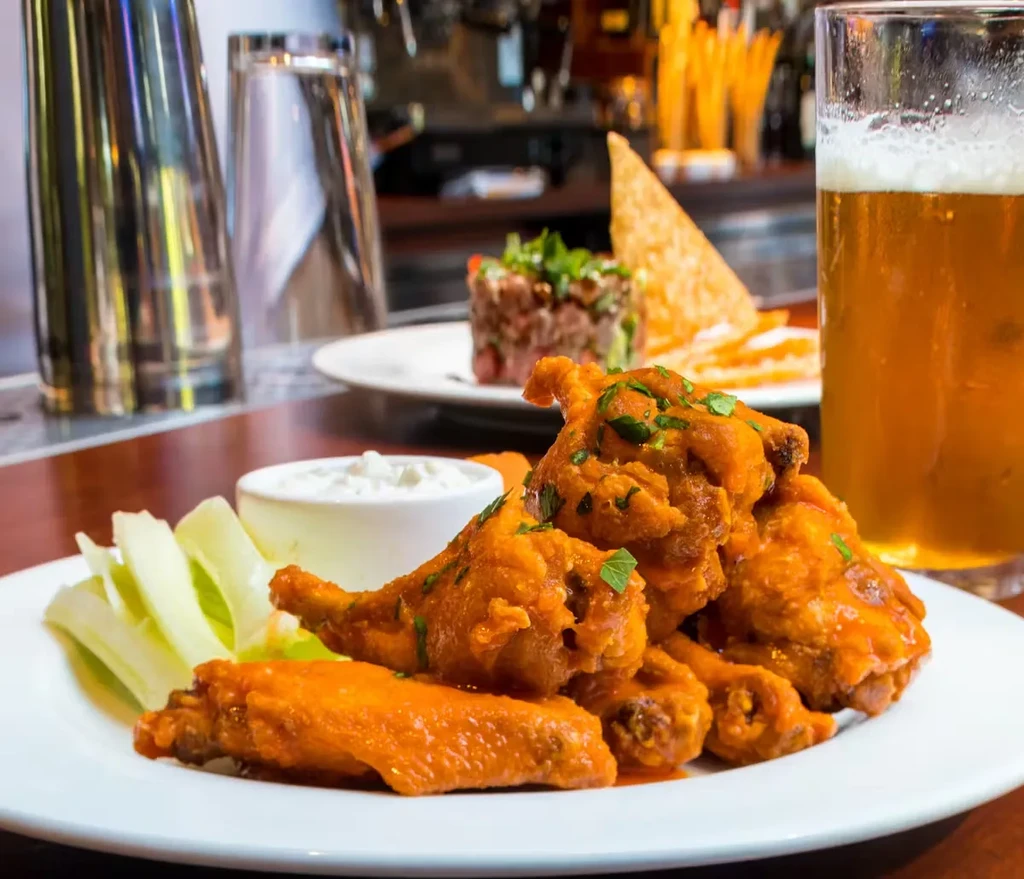 A plate of buffalo wings with celery, dipping sauce, and beer.