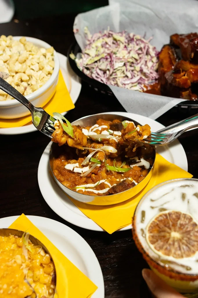 A table with plates of baked beans, macaroni, coleslaw, and a cocktail.