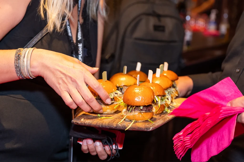A server holding a tray of mini-burgers, with a person taking one.