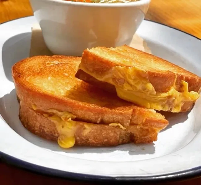 Two halves of a grilled cheese sandwich with melted cheese dripping out.