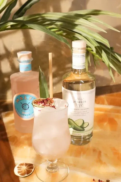 A pink cocktail with two spirit bottles and a palm leaf.