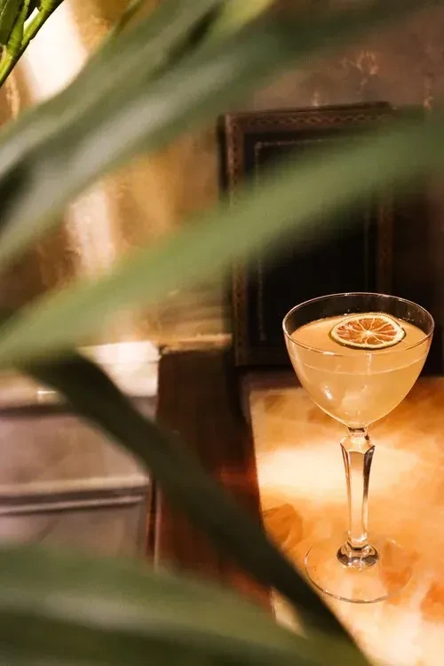 A cocktail in a coupe glass with a lime slice on a marble table.