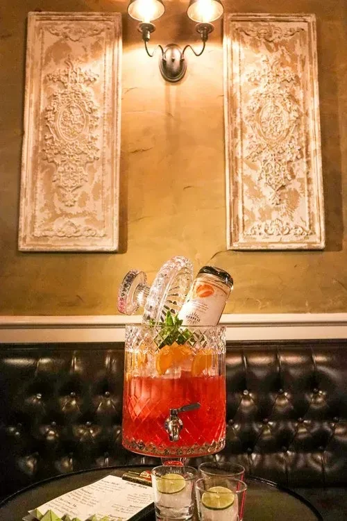 A large crystal drink dispenser filled with a red cocktail on a table.