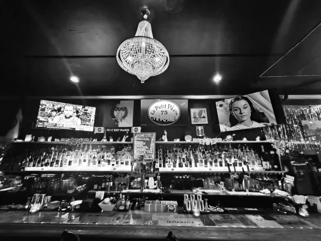 Black-and-white image of a bar with a large chandelier and several screens.