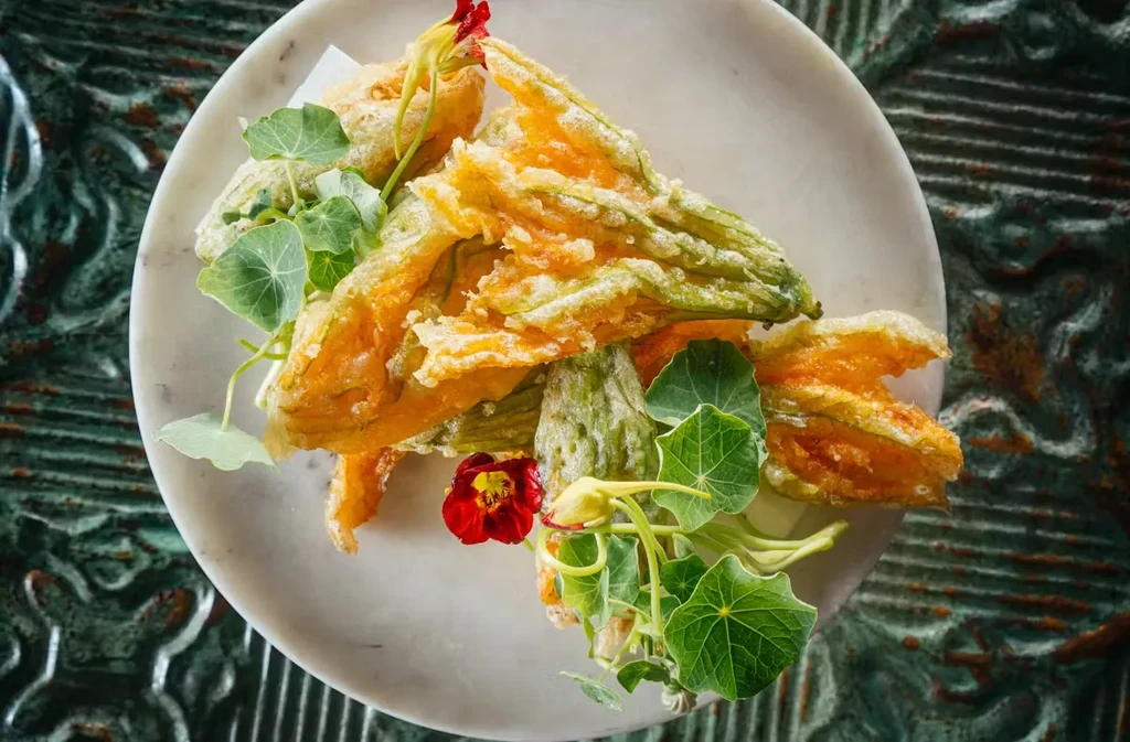 Fried squash blossoms on a white plate with edible flowers and greens.