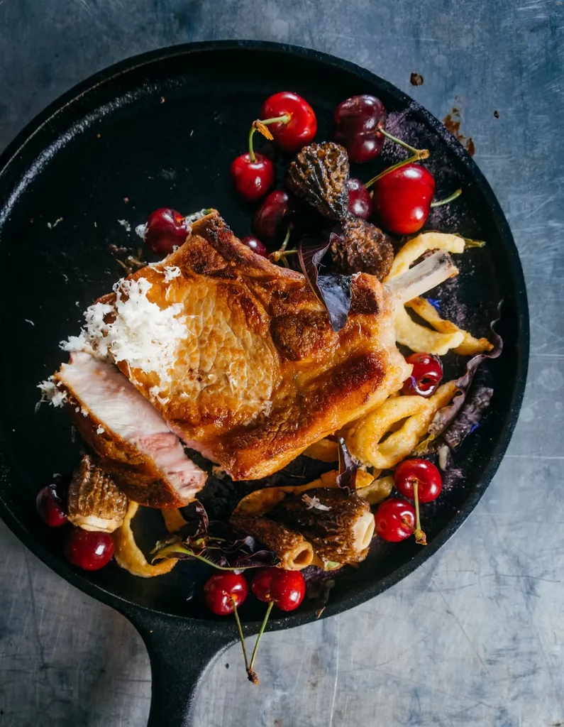 Pork chop with cherries and mushrooms in a black skillet.