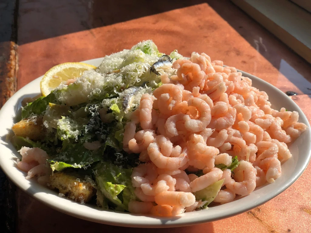 A white plate filled with Caesar salad, shrimp, and anchovies.