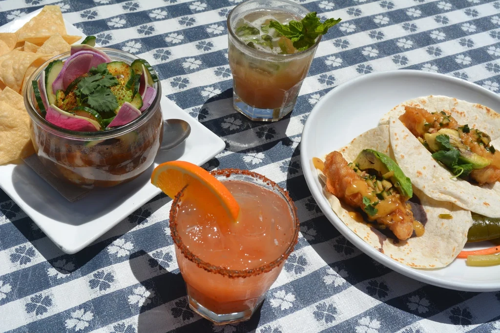 Three drinks and a fish taco meal on a checkered tablecloth.