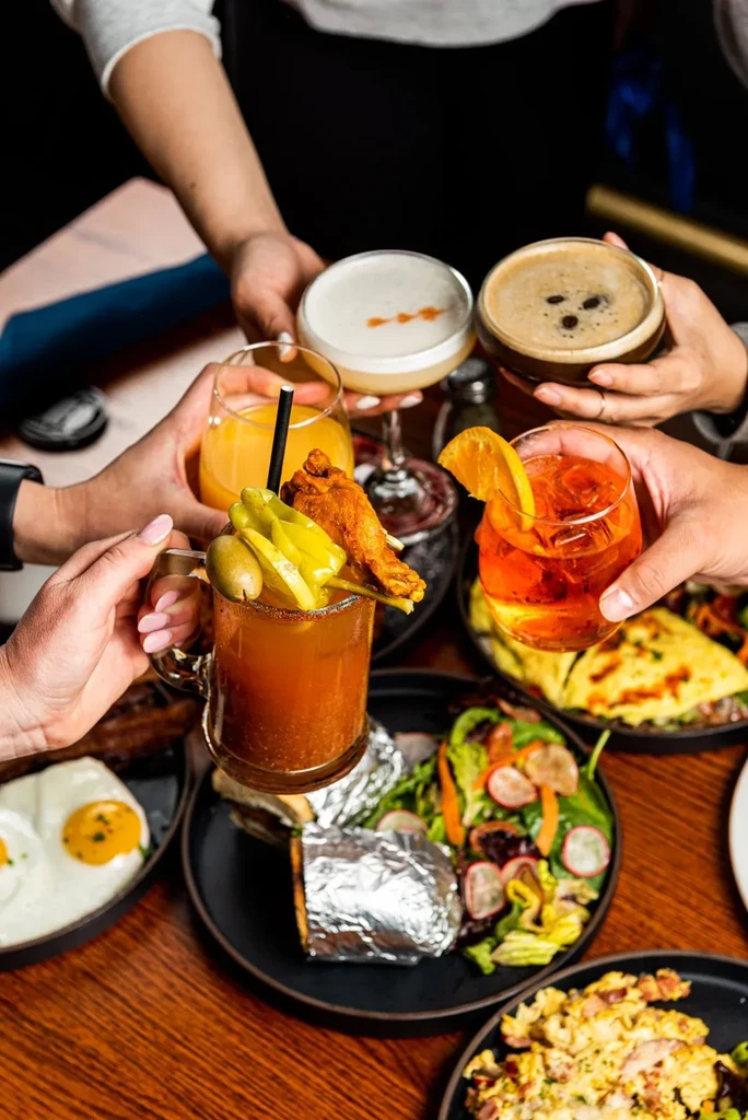 Five people toast various beverages and brunch dishes.