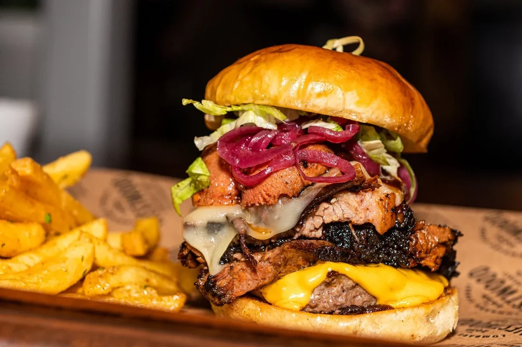 A large loaded burger with fries on a paper-lined tray.