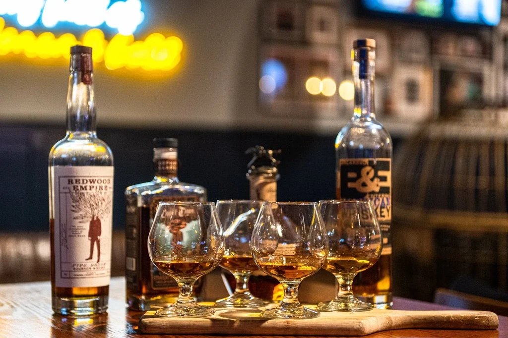 A whiskey tasting with four glasses and three bottles on a wooden board.